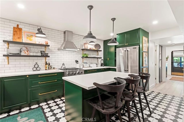 kitchen with appliances with stainless steel finishes, decorative backsplash, green cabinetry, wall chimney exhaust hood, and a breakfast bar