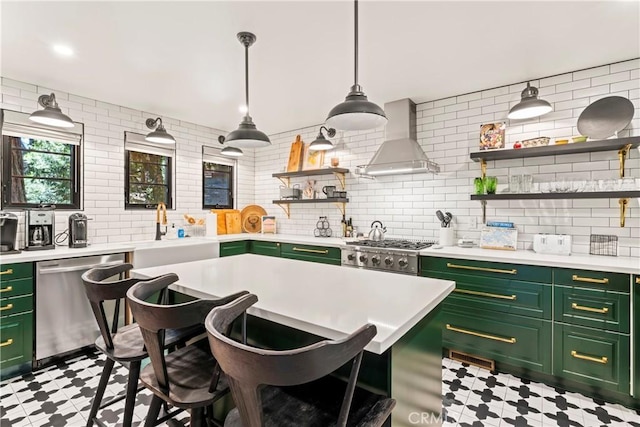 kitchen with wall chimney exhaust hood, stainless steel appliances, backsplash, green cabinets, and a breakfast bar area