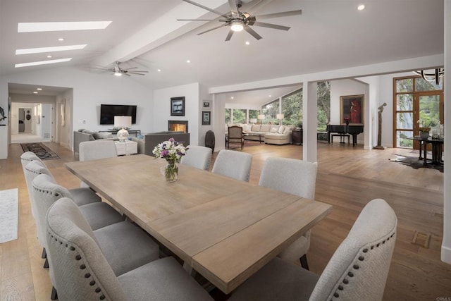 dining room with ceiling fan, light wood-type flooring, and vaulted ceiling with skylight