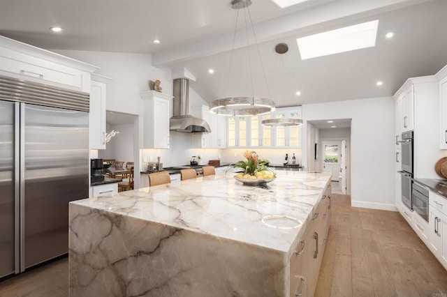 kitchen featuring light stone counters, wall chimney exhaust hood, pendant lighting, stainless steel appliances, and a spacious island