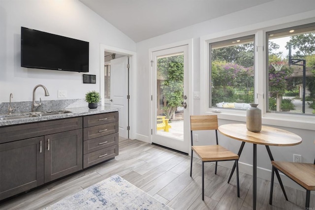 interior space featuring sink, lofted ceiling, dark brown cabinets, and light stone countertops