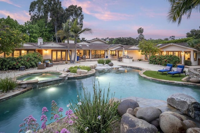 pool at dusk featuring an in ground hot tub and a patio