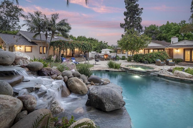 pool at dusk with pool water feature, an in ground hot tub, and a patio