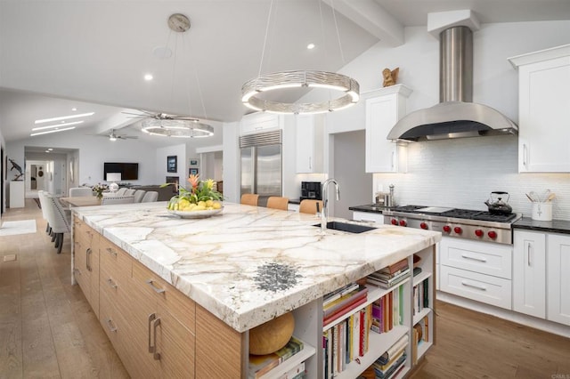 kitchen with wall chimney exhaust hood, stainless steel appliances, an island with sink, tasteful backsplash, and sink