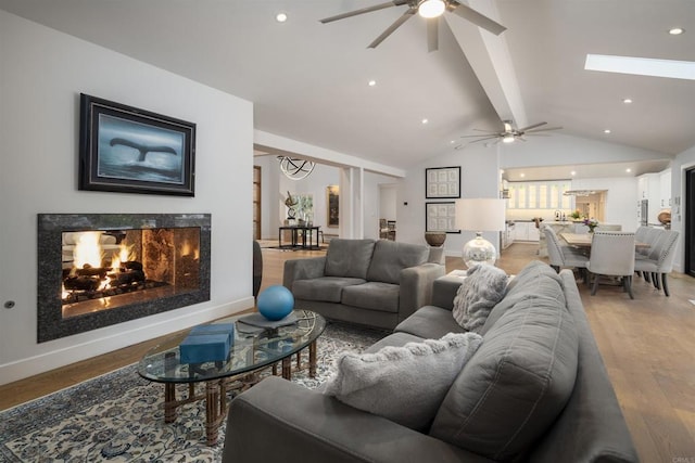 living room with ceiling fan, a fireplace, hardwood / wood-style floors, and vaulted ceiling with beams