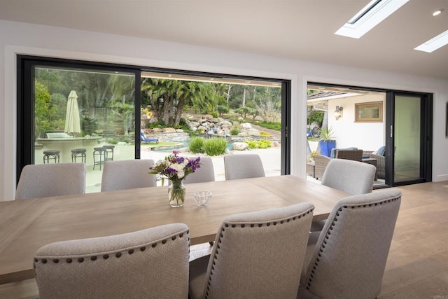 dining room with vaulted ceiling with skylight and light hardwood / wood-style floors