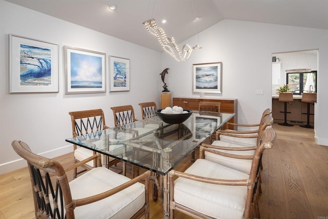 dining space with a chandelier, light wood-type flooring, and vaulted ceiling