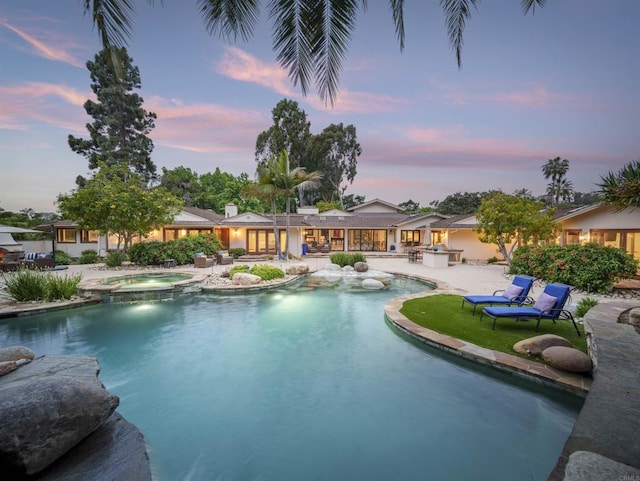 pool at dusk with a patio area and an in ground hot tub