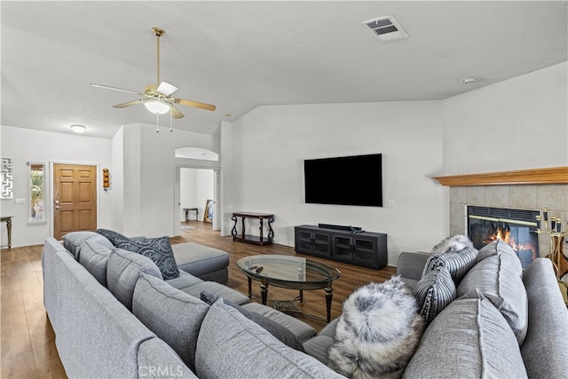 living room featuring ceiling fan, vaulted ceiling, dark wood-type flooring, and a tile fireplace