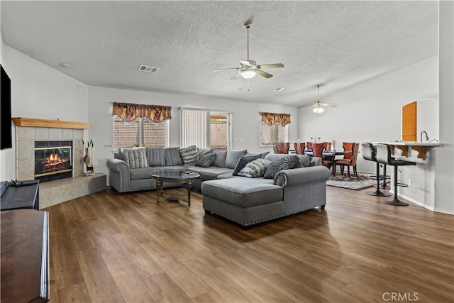 living room featuring hardwood / wood-style floors, a textured ceiling, vaulted ceiling, ceiling fan, and a tiled fireplace