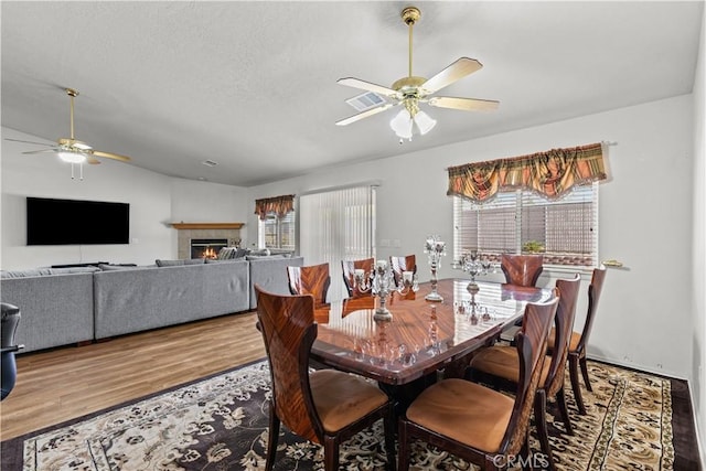 dining space featuring ceiling fan, lofted ceiling, a tile fireplace, and hardwood / wood-style flooring