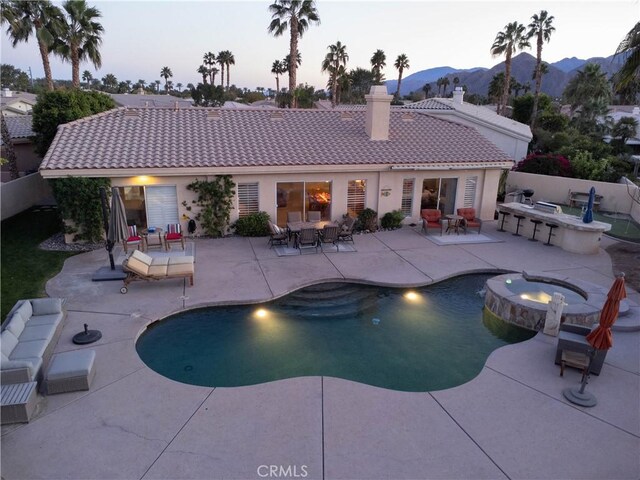 pool at dusk featuring a mountain view, an in ground hot tub, and a patio