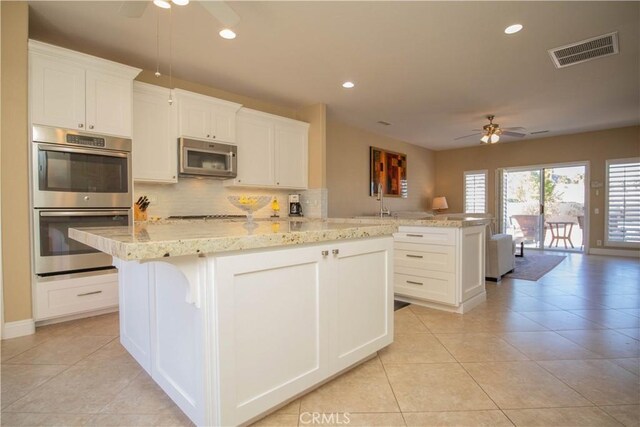 kitchen with white cabinetry, kitchen peninsula, stainless steel appliances, decorative backsplash, and a center island