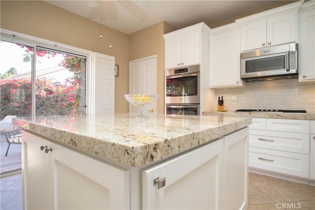 kitchen with light tile patterned floors, appliances with stainless steel finishes, backsplash, white cabinets, and light stone counters