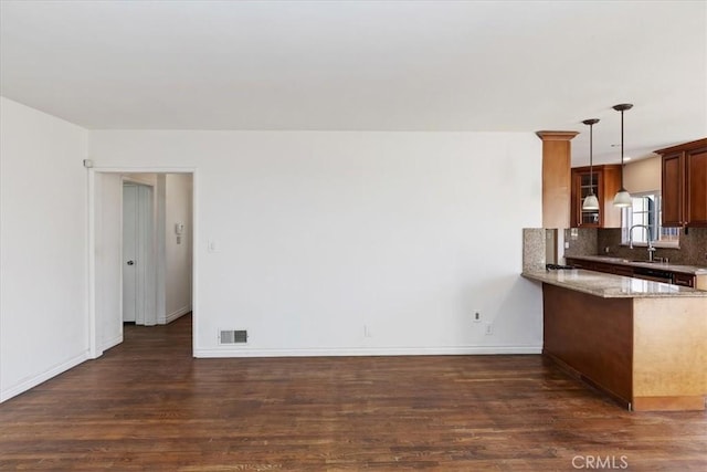 kitchen featuring kitchen peninsula, hanging light fixtures, backsplash, dark hardwood / wood-style flooring, and sink