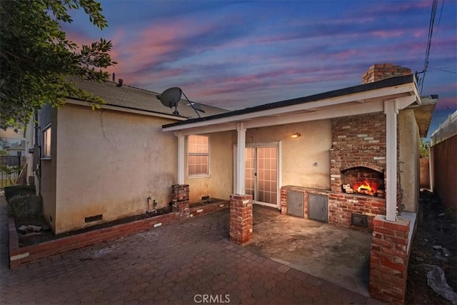 back house at dusk featuring an outdoor fireplace and a patio