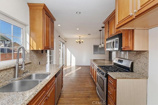 kitchen with sink, decorative light fixtures, light stone counters, and appliances with stainless steel finishes