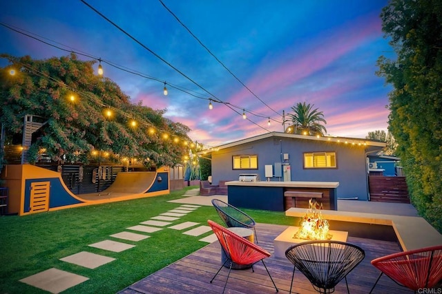 rear view of house featuring an outdoor fire pit, a lawn, a deck, and stucco siding