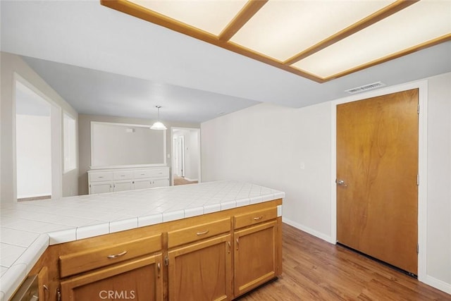 kitchen with kitchen peninsula, tile counters, pendant lighting, and light hardwood / wood-style flooring