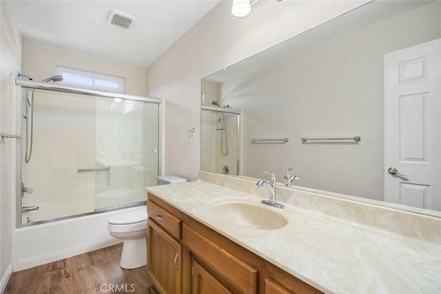 full bathroom with combined bath / shower with glass door, vanity, hardwood / wood-style flooring, and toilet