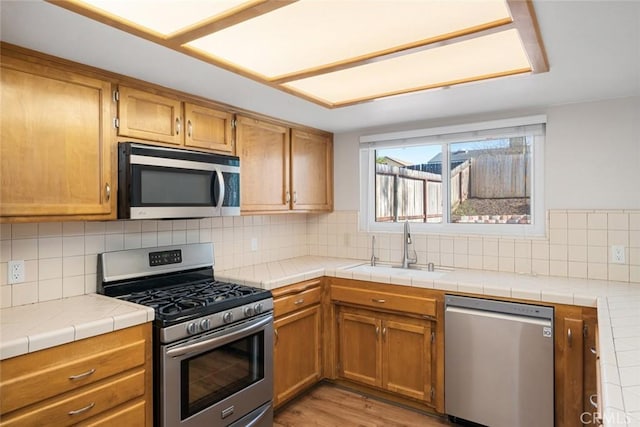 kitchen with appliances with stainless steel finishes, backsplash, sink, and tile counters