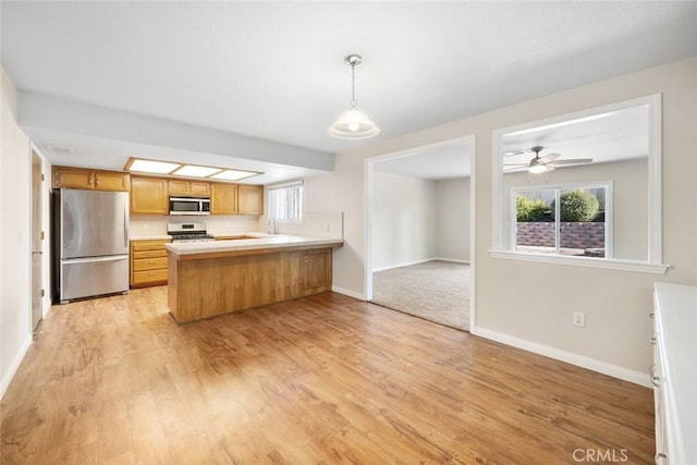 kitchen featuring kitchen peninsula, light hardwood / wood-style flooring, hanging light fixtures, stainless steel appliances, and decorative backsplash