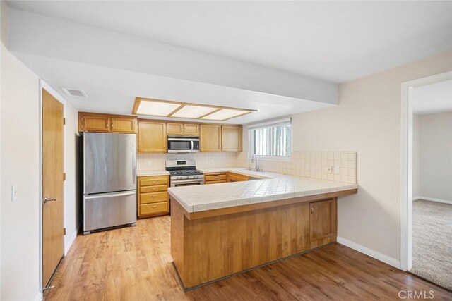 kitchen featuring appliances with stainless steel finishes, kitchen peninsula, tile countertops, sink, and light hardwood / wood-style flooring