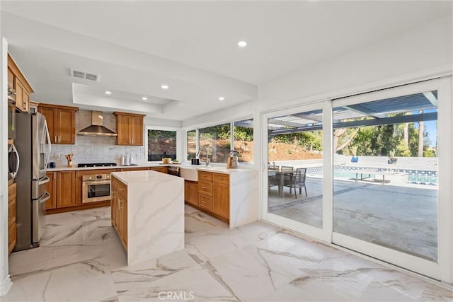 kitchen featuring stainless steel appliances, sink, tasteful backsplash, wall chimney range hood, and a tray ceiling