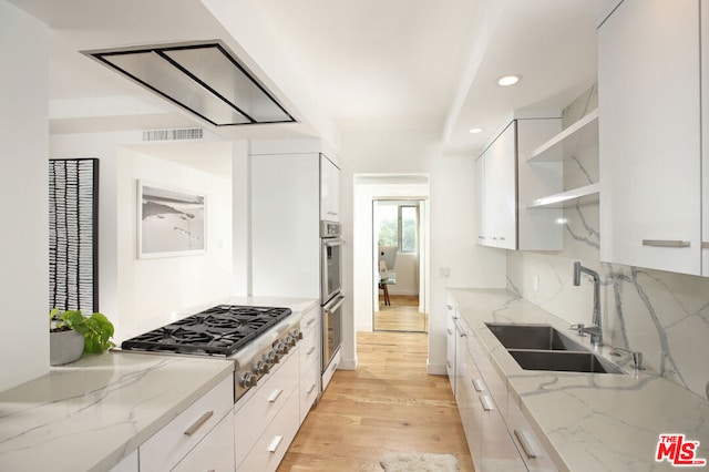 kitchen featuring sink, white cabinetry, light wood-type flooring, stainless steel appliances, and light stone countertops