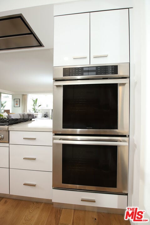 interior details featuring stainless steel double oven, white cabinets, and light wood-type flooring