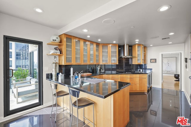 kitchen featuring a kitchen breakfast bar, kitchen peninsula, sink, wall chimney range hood, and backsplash