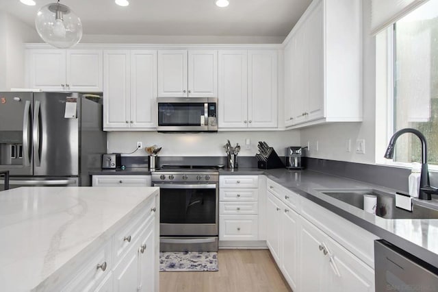 kitchen with appliances with stainless steel finishes, a healthy amount of sunlight, dark stone counters, white cabinets, and sink