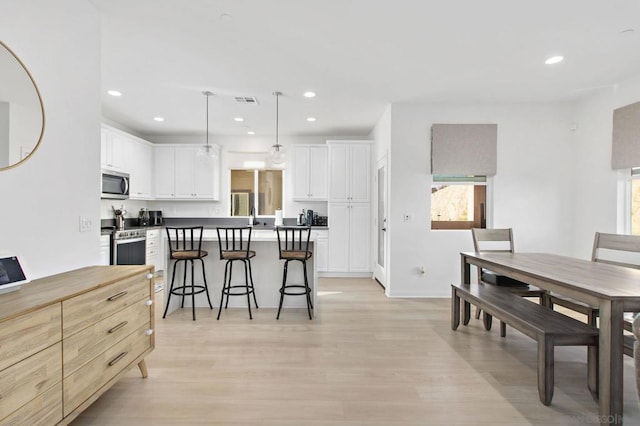 kitchen featuring white cabinets, light wood-type flooring, appliances with stainless steel finishes, and pendant lighting