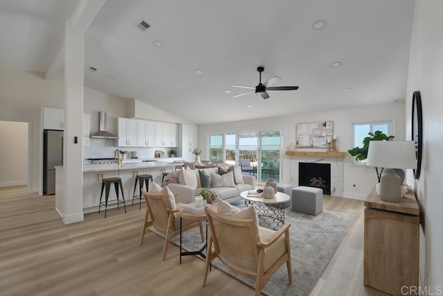 living room with lofted ceiling, light wood-type flooring, a high end fireplace, and ceiling fan