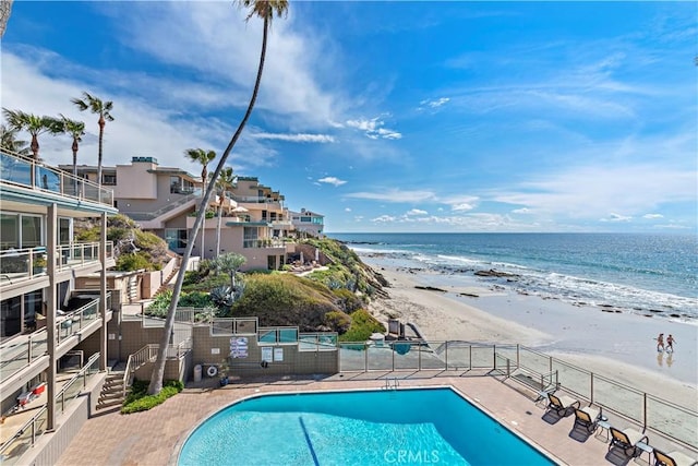 view of swimming pool with a water view, a view of the beach, and a patio area