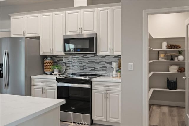 kitchen with white cabinets, stainless steel appliances, hardwood / wood-style floors, and backsplash