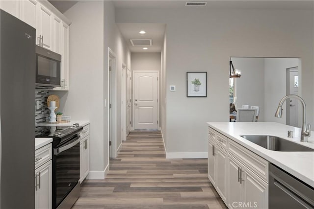 kitchen featuring stainless steel appliances, decorative backsplash, white cabinetry, wood-type flooring, and sink