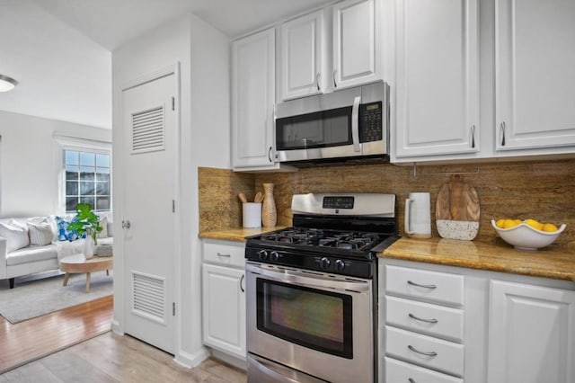 kitchen featuring decorative backsplash, stainless steel appliances, white cabinets, and light wood-type flooring