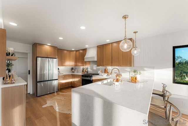 kitchen featuring pendant lighting, kitchen peninsula, stainless steel refrigerator, custom range hood, and gas range