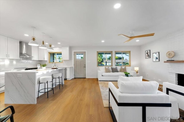 living room with sink, a brick fireplace, ceiling fan, and light hardwood / wood-style flooring