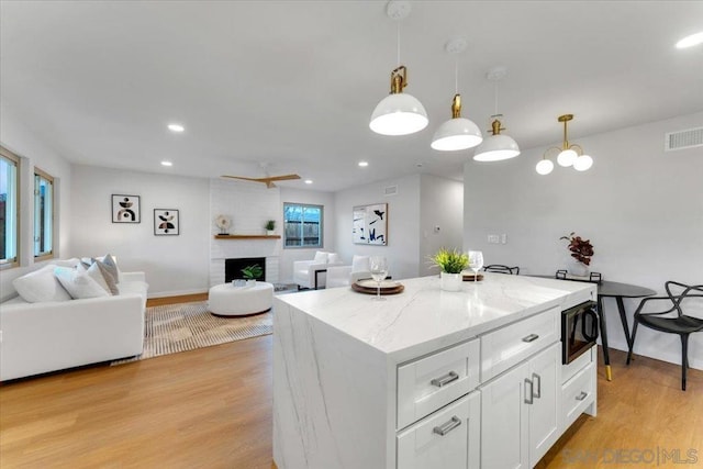 kitchen with decorative light fixtures, a brick fireplace, light wood-type flooring, white cabinets, and black microwave