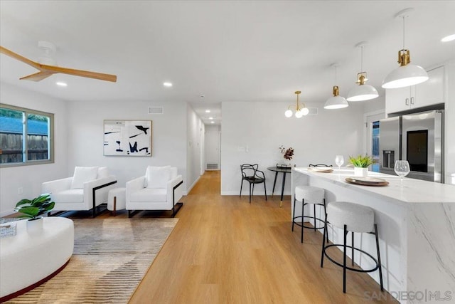 living room with light wood-type flooring and ceiling fan with notable chandelier