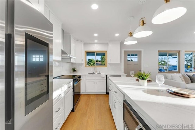 kitchen featuring stainless steel refrigerator, black range with electric stovetop, sink, white cabinetry, and decorative light fixtures