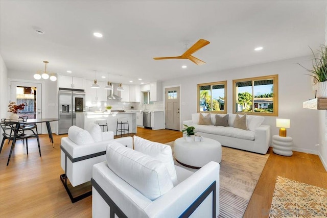 living room with light hardwood / wood-style floors, sink, and ceiling fan with notable chandelier