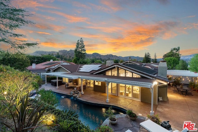 back house at dusk featuring a patio, outdoor lounge area, a mountain view, cooling unit, and solar panels