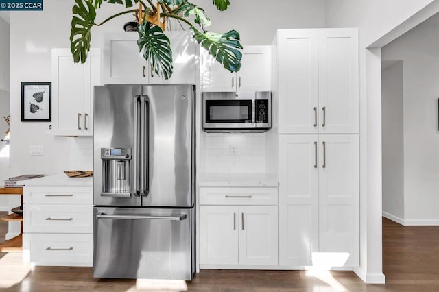 kitchen with light stone countertops, appliances with stainless steel finishes, dark wood-type flooring, white cabinetry, and tasteful backsplash