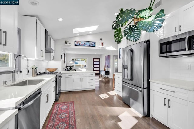 kitchen featuring appliances with stainless steel finishes, sink, white cabinets, vaulted ceiling with skylight, and decorative backsplash