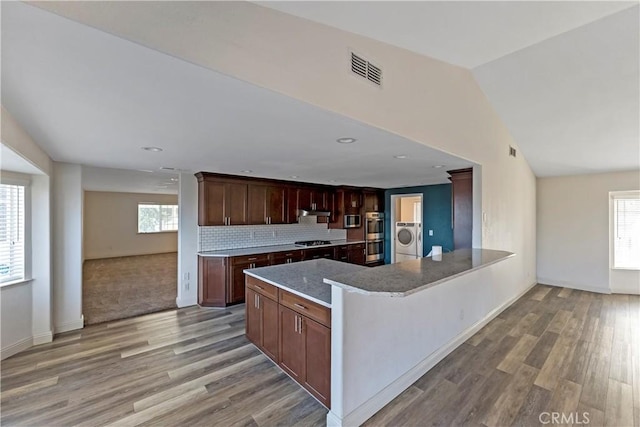 kitchen with washer / dryer, lofted ceiling, light hardwood / wood-style floors, and backsplash