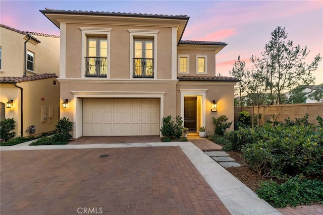 mediterranean / spanish-style house featuring an attached garage, fence, a tiled roof, decorative driveway, and stucco siding