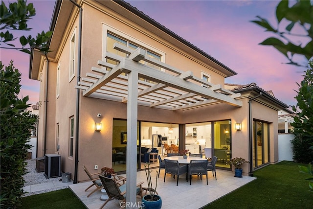 back house at dusk featuring central air condition unit, a pergola, and a patio area